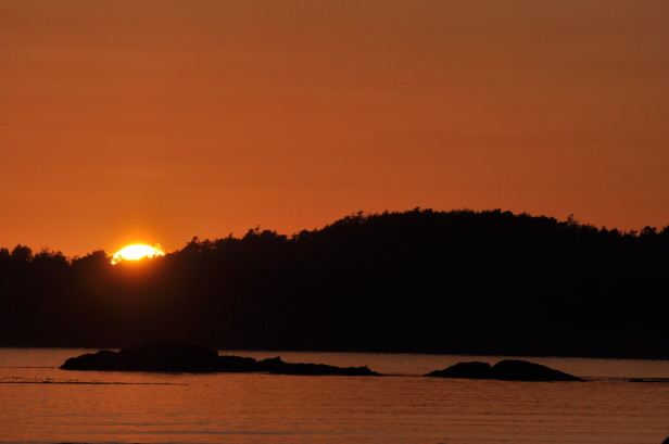 Sun sets behind a small island at the beach in Tofino, BC. 