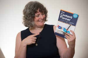 Author Angela Crocker holding a copy of The Content Planner. Her head is turned to look at the book and she smiles as you points to it.