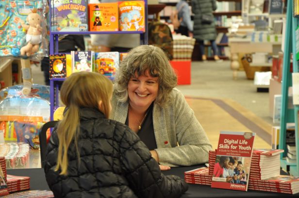 Author Angela Crocker seated at a table in a bookstore talking to a tween age girl. Copies of Digital Life Skills for Youth are on the table.