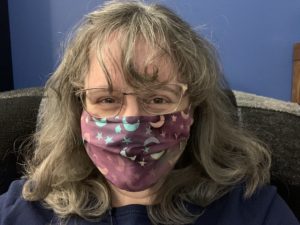 Angela Crocker with long, dark blonde hair, looks at the camera wearing a fabric facemask with a stars and moons print from Bamboobino; one of Angela's online shopping purchases