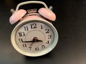 A vintage analog alarm clock with white face, black numbers, and pink bells to illustrate time, talent, and treasure.